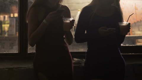 Two attractive girls checking social networks, drinking cocktails at party