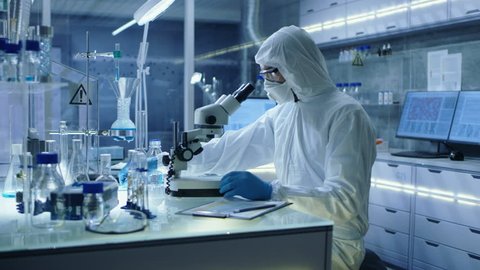 In a Secure High Level Research Laboratory Scientist in a Coverall Adjusts Samples in a Petri Dish with Pincers and then Examines Them Under Microscope.  Shot on RED EPIC-W 8K Helium Cinema Camera.