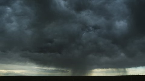 Massed gray clouds spilling rain roll away across the prairie, time lapse