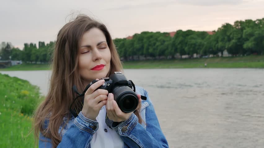 Beautiful girl tourist taking photos with a professional camera on the banks of the river in windy weather