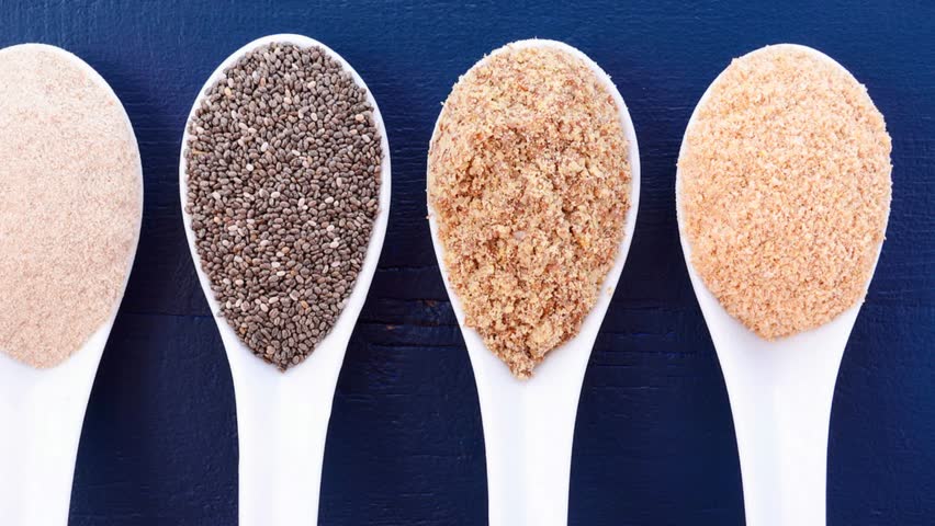 High fiber nutritious grains including white grain quinoa, psyllium husk powder, black chia, wheat germ, and ground LSA mix, in measuring spoons, panning shot.  Royalty-Free Stock Footage #26667529