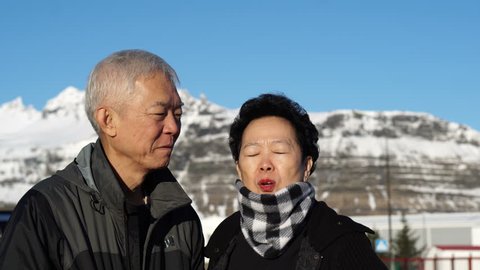 Cute Asian senior elder couple happy honeymoon anniversary trip in Europe snow alp. Kissing on cheek