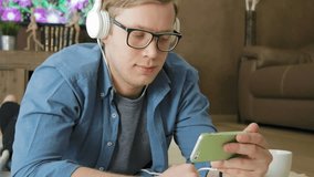 Young laughing man watching streaming movie on smartphone eating cereals with headphones