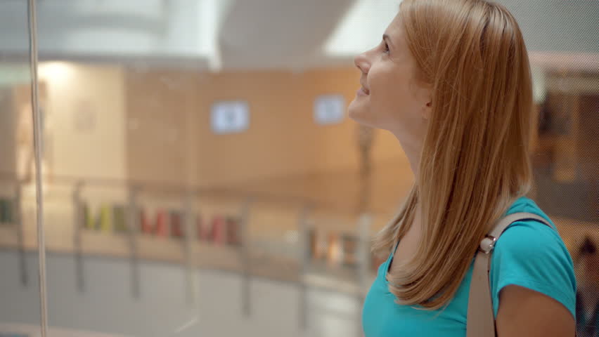 Happy smiling young woman in turquoise t-shirt riding in shopping center elevator looking up