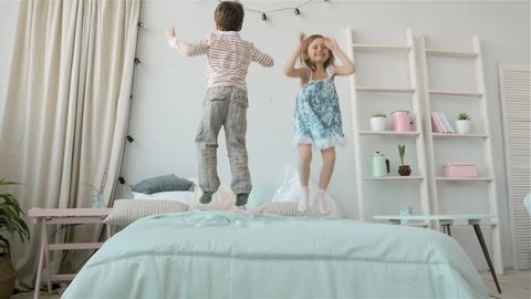 Portrait of children jumping on a bed, little boy and girl brother and sister have fun and laughing, happy kids on quarantine, coronavirus home isolation