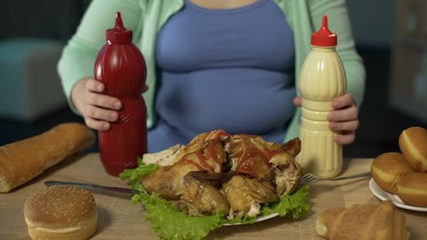 Obese female adding lots of unhealthy ketchup and mayonnaise to roast chicken, poor nutrition habit, junk food addiction. Fat woman having unhealthy dinner at home, diet, weight loss problem, calories