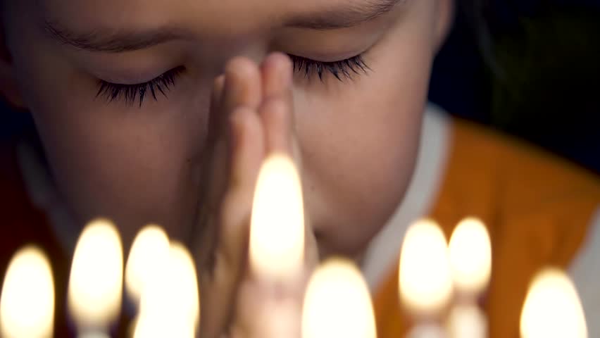 Small child girl praying to God in the temple on the eyelashes tears in front of lit candles