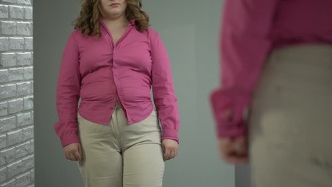 Lady buttoning up her shirt on stomach with great effort, obesity health problem