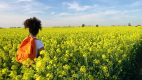 4K video clip of beautiful happy mixed race African American girl teenager female young woman hiking with an orange backpack yellow flowers