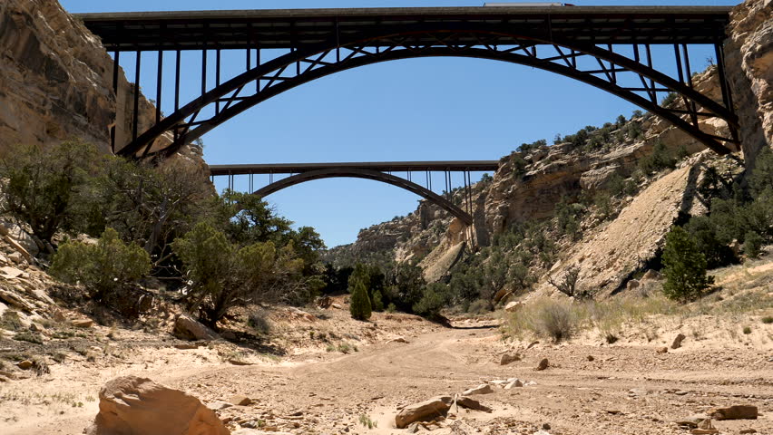 Side by side off road vehicle drives away on the trail along the bottom of Eagle Canyon in the San Rafael Swell desert passing under twin freeway bridges of Interstate 70 spanning the canyon.