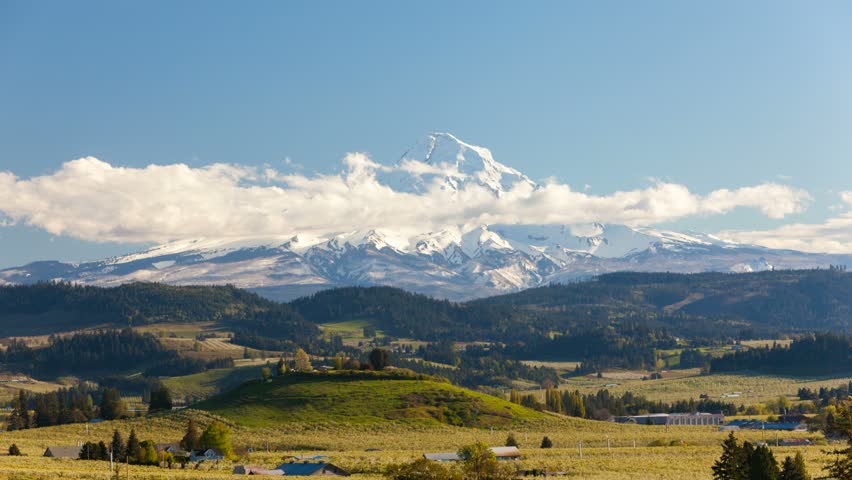 Time lapse movie of moving clouds and sky over snow covered Mt. Hood and rolling hills landscape pear orchards in Hood River Oregon spring season 4k uhd