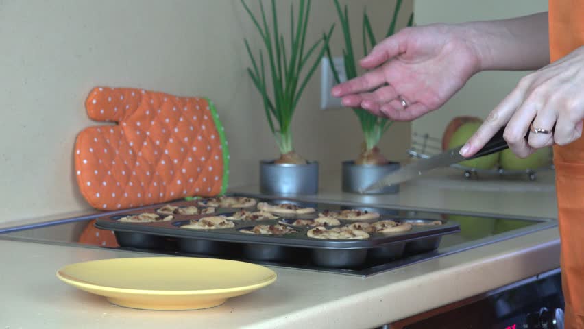 woman hands take out baked meat cup cakes from cookie sheet and put in yellow dish. Static closeup shot.