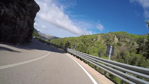 Driving lots of curves on mountain roads with a motorcycle resp. motorbike through summer landscape on Sardinia in Italy.
