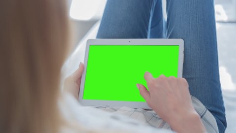 Young Woman laying on a couch uses tablet PC with pre-keyed green screen. Few types of motion - scrolling up and down, tapping, zoom in and out. Perfect for screen compositing. 10bit ProRes 444
