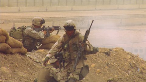 Marines advancing over Iraqi terrain, firing automatic weapons