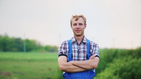 Portrait of a happy man in overalls in nature. Young attractive happy man looking at the camera in the meadow. Handheld shot.