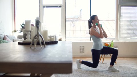 young fit and energetic woman doing sport workout and fitness lunge exercises with weights for healthy lifestyle in living room at home during sunny day