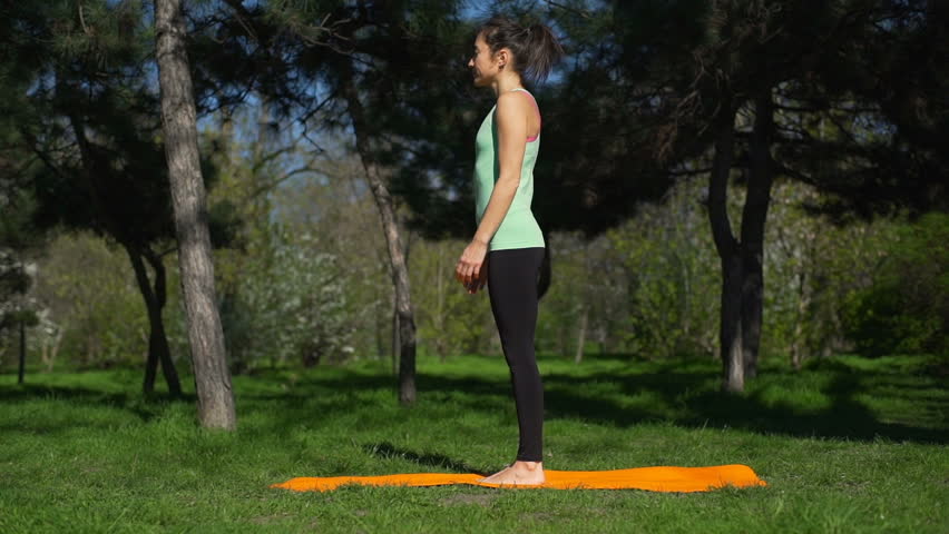 Young beautiful woman does yoga on the yellow carpet in the park slow motion