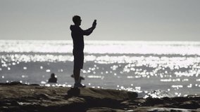 Man on a beach is taking a picture of an ocean