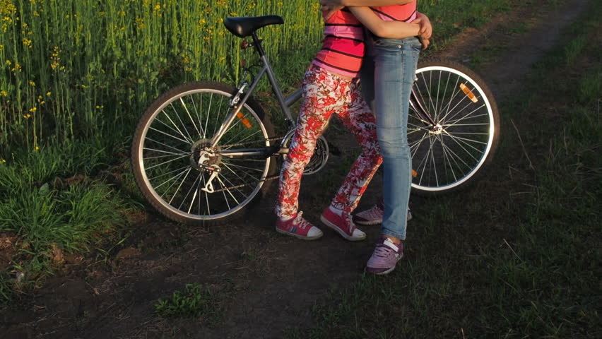 A woman with a child watching the sunset. A sports family with a bicycle. Mom hugs her daughter. Countryside.