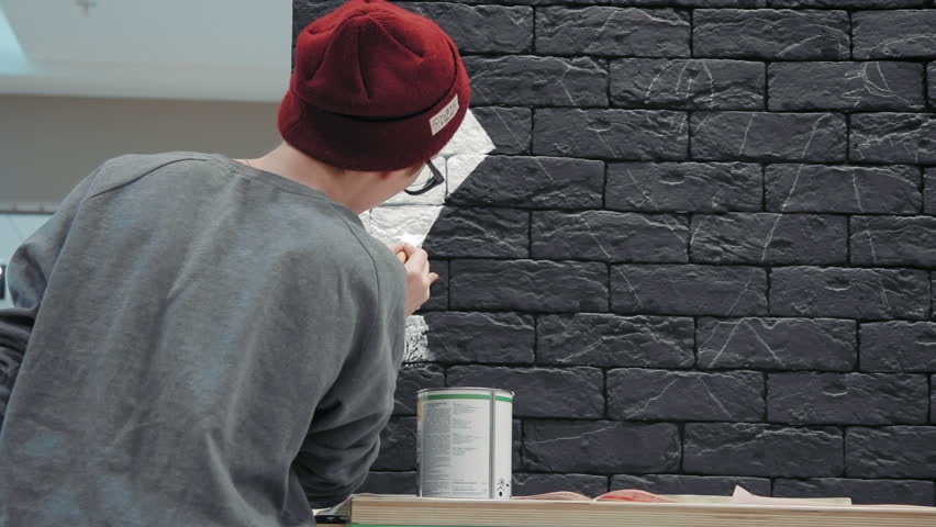 Creative painter Rear view Young female painter making white design on the black brick wall in coffee shop