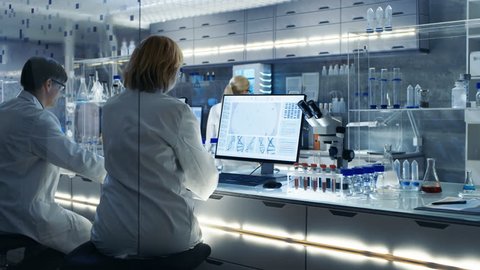 Senior Female Scientist Works with High Tech Equipment in a Modern Laboratory. Her Colleagues are Working Beside Her. Shot on RED EPIC-W 8K Helium Cinema Camera.