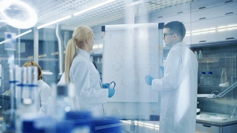 Young Female and Male Scientists Write Formulas on a Whiteboard. They're Solving Scientific Problems in Bright Modern High Tech Laboratory. Shot on RED EPIC-W 8K Helium Cinema Camera.
