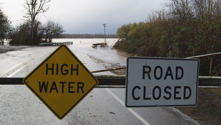 High Water and Road Closed signs on a barricade in front of a flooded road and bridge