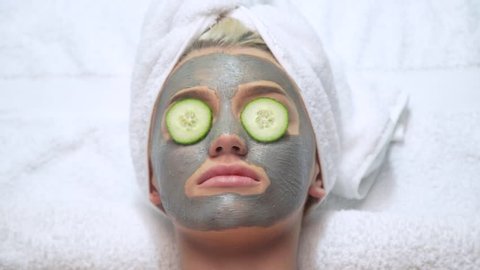 Attractive young blonde model wearing face mask with cucumber on her eyes and towel on her head