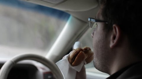 Man Eating a Burger at the Wheel of a Car. Unhealthy Food