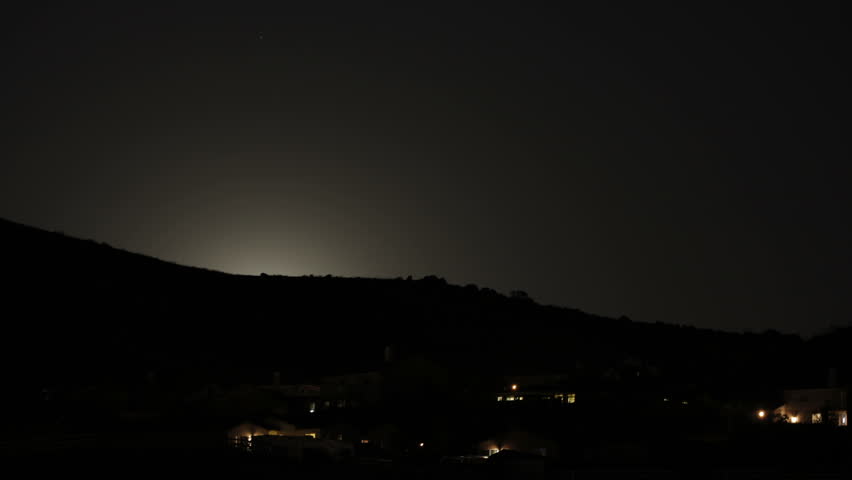 A moon rising over a residential hill in time-lapse