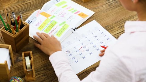 Businesswoman Marking A Date On Calendar After Looking The Schedule From Diary On Office Desk