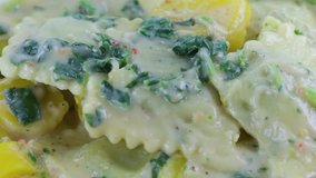 A very close video of a spinach ravioli TV dinner with vegetables being slowly mixed with a fork.
