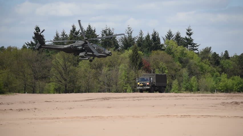 A military helicopter is flying by over rough terrain.