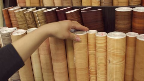 Girl looking at linoleum flooring in interior store, close-up. Racks with linoleum rolls in wholesale warehouse.