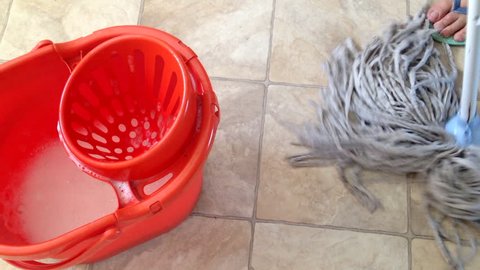 High shot of a hand mop cleaning a linoleum floor with a mop bucket.