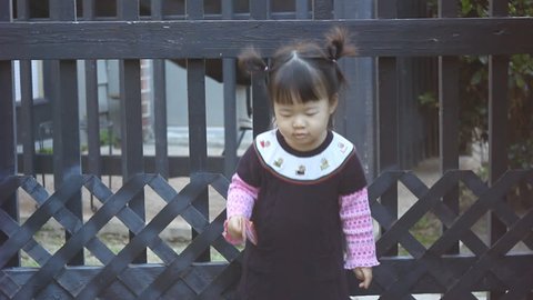 Beautiful East Asian Girl Toddler in purple outfit in front of black lattice gate