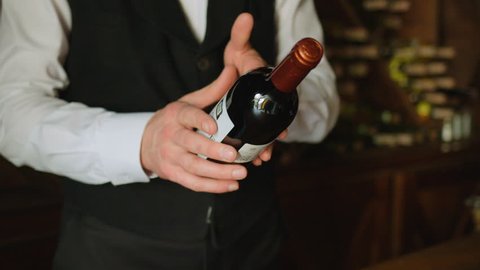 Attractive sommelier puting botlle of wine from hand to hand on the wood background with wine. Slow motion. Close up.