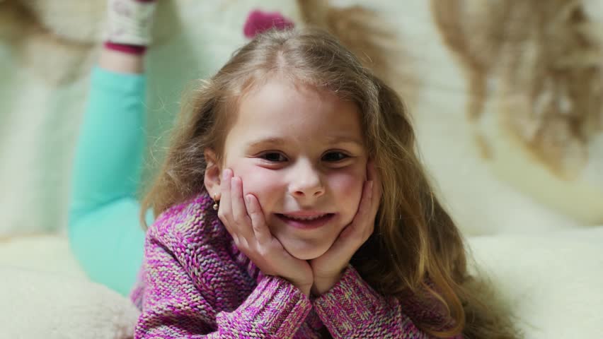 Beautiful little girl smiling at camera. Portrait of cheerful kid lying on couch
