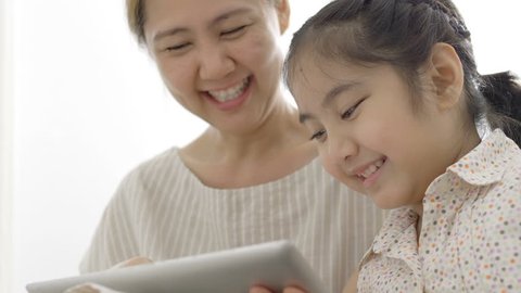 4K : Slow motion of Happy Asian mother and daughter playing with digital tablet together at home, Tilt up shot