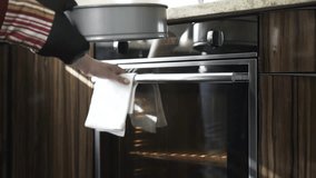 Close up of an unrecognizable woman putting dough in a gray form into an oven and setting the time. Locked down real time close up shot