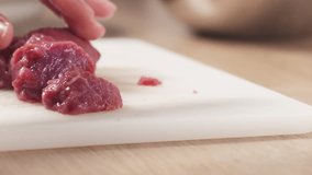 Slow motion slide shot of young female hand cutting raw beef with a knife on plastic board, 180fps prores footage