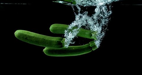Long Courgette or Zucchini, cucurbita pepo, Vegetable falling into Water against black background, slow motion 4K