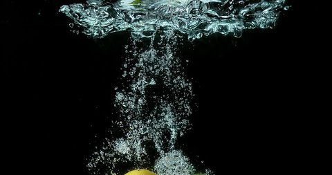 Yellow and Green Lemons, citrus limonum, Citrus aurantifolia, Fruits falling into Water against Black Background, Slow Motion 4K