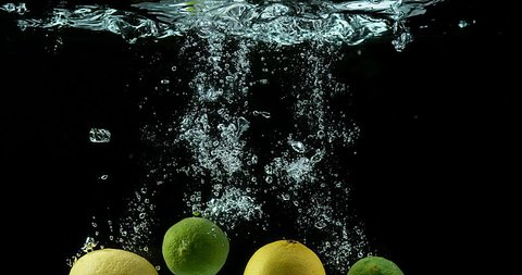 Yellow and Green Lemons, citrus limonum, Citrus aurantifolia, Fruits falling into Water against Black Background, Slow Motion 4K