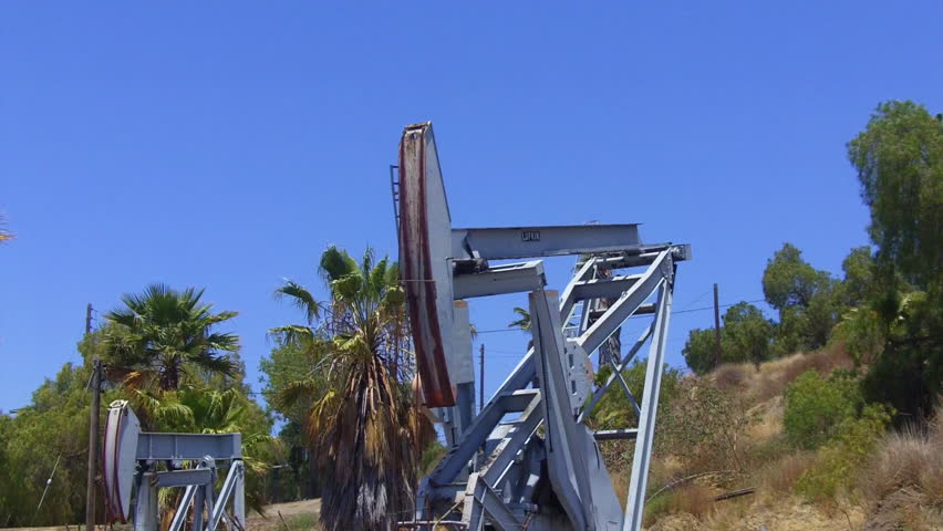 A low angle shot of two oil well jacks derricks pumps extracting petroleum from