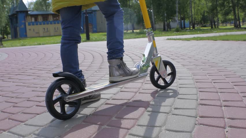 Little girl in green jacket and jeans riding a scooter on the sidewalk. Shooting Steadicam.