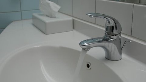 Water running continuously from water tap. White bathroom sink.