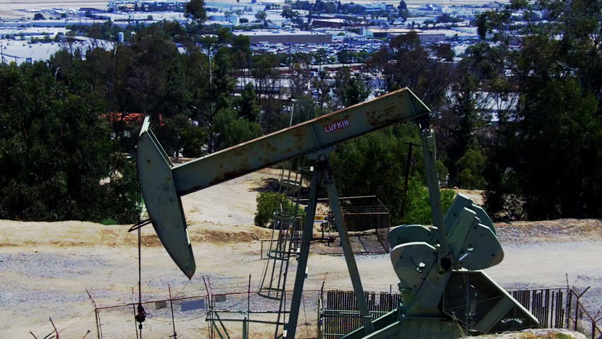 An oil well pumping rig in the foreground and an urban Los Angeles landscape