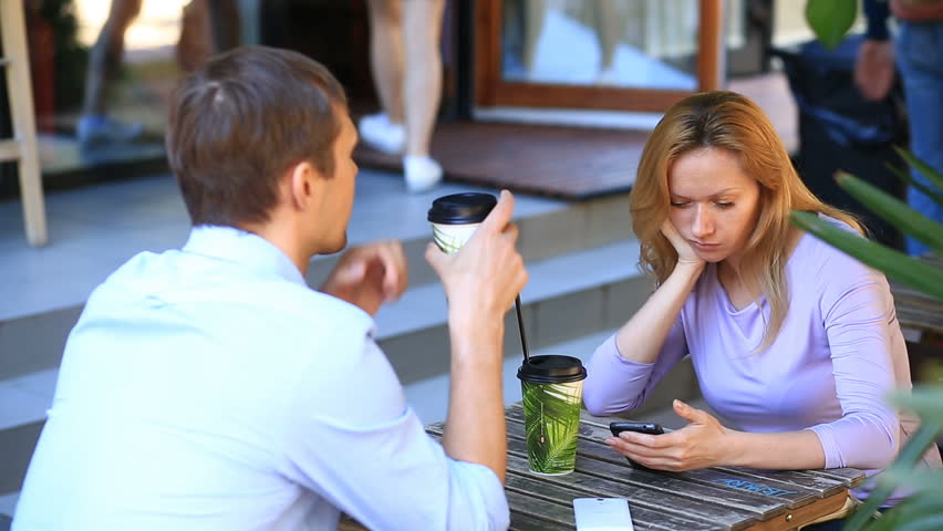 couple in love in an outdoor cafe. Man and beautiful woman on a date. Everyone is looking at his mobile phone